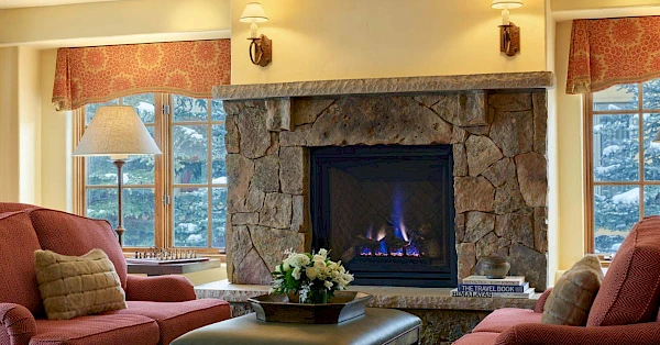 A cozy living room with a stone fireplace, red sofas, large windows, and a coffee table topped by a floral arrangement. Always ending the sentence.