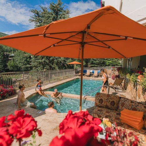 An outdoor seaside cafe with orange umbrellas, colorful flowers, and blue sky; a relaxing waterfront dining spot.