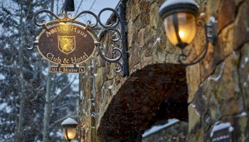 Snowy stone street with vintage hanging sign for a club and hotel, warm lanterns glowing along an arched doorway.
