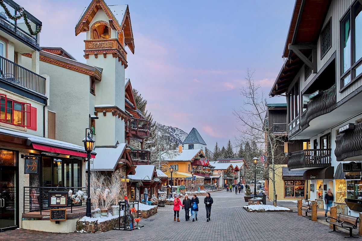 A charming pedestrian street in a snowy mountain village, lined with cafes, shops, and timbered chalets, with a clock tower rising over the scene.